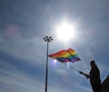Man Waving Rainbow LGBT Flag with Lamp and Sun in Background During Parade