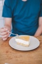 Man wear blue t-shirt sitting in coffee shop eating lemon cheesecake in white plate with folk