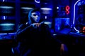 Man wear white mask look like hacker and point to front in room and monitor show light with sign look fear and scary in background