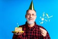 man wearing birthday hat with cake isolated on bright blue colour background, studio portrait Royalty Free Stock Photo
