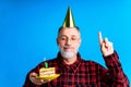 man wearing birthday hat with cake isolated on bright blue colour background, studio portrait Royalty Free Stock Photo