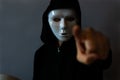 Man wearing a black hood and a white anonymous mask pointing with his finger Royalty Free Stock Photo