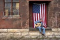Man wearing blue jeans playing acoustic guitar on warehouse loading dock with American flag