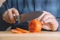 Man wearing a blue shirt slicing a tomato on a wooden board. Cooking concept