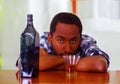 Man wearing blue white shirt sitting by bar counter lying over desk next to glass and bottle, depressed facial Royalty Free Stock Photo