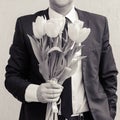 A man wearing a business suit, holding a bouquet of tulips. The man gives a bouquet of flowers.