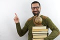 Man wearing casual clothes and glasses holding pile of books and vintage world ball smiling happy pointing with hand and finger to Royalty Free Stock Photo