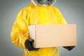 Man wearing chemical protective suit with cardboard box on grey background, closeup. Prevention of virus spread Royalty Free Stock Photo