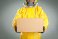 Man wearing chemical protective suit with cardboard box on grey background, closeup. Prevention of virus spread Royalty Free Stock Photo