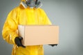 Man wearing chemical protective suit with cardboard box on light grey background. Prevention of virus spread Royalty Free Stock Photo