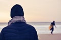 Man wearing coat, scarf and knit cap in front of the ocean
