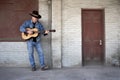 Man wearing cowboy hat, blue jeans playing guitar on factory loading