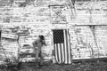 Man wearing cowboy hat standing in front of old abandoned barn with American flag Royalty Free Stock Photo