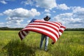 Man wearing cowboy hat standing in grass field, holding American flag blowing in wind behind him