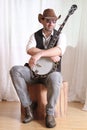 Man wearing cowboy leather hat and sunglasses holding banjo with crossed arms