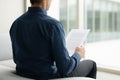Man in Blue Shirt Reading Document on Couch with City View in Bright Office Interior Royalty Free Stock Photo