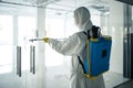 A man wearing disinfection suit spraying with sanitizer the glass doors` handles in an empty shopping mall to prevent covid-19