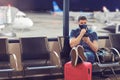 Man wearing face mask sitting in airport departure terminal using mobile phone tracking app while waiting for boarding