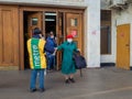 A man wearing a face mask and uniform distributes newspapers to people exiting the doors of a subway station