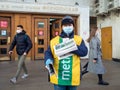 A man wearing a face mask and uniform distributes newspapers to people exiting the doors of a subway station