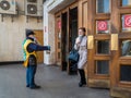 A man wearing a face mask and uniform distributes newspapers to people exiting the doors of a subway station