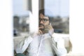 Man wearing glasses making a  mobile phone call sitting down looking through the window Royalty Free Stock Photo