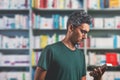 man wearing glasses reading the cover of a book in the library