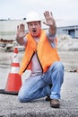 Man wearing hard hat and safety vest kneeling next to traffic cone, holding hands up and yelling to stop Royalty Free Stock Photo