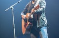 Man wearing leather jacket playing acoustic guitar on stage