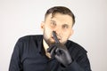 A man wearing medical gloves puts his index finger to his lips and makes