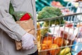 A man wearing medical gloves and a shopping bag with fresh vegetables, over blurred shopping cart with healths products. Concept