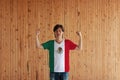 Man wearing Mexico flag color of shirt and standing with raised both fist on the wooden wall background, a vertical tricolor of Royalty Free Stock Photo