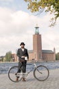 Man wearing old fashioned black suit and hat holding a vintage bicycle in front of Stockholm City Hall Royalty Free Stock Photo