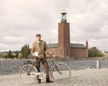 Man wearing old fashioned tweed suit and hat holding a retro bicycle in front of Stockholm City Hall Royalty Free Stock Photo