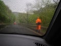 The man is wearing an orange raincoat. The road is under repair