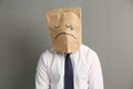 Man wearing paper bag with drawn sad face on grey background Royalty Free Stock Photo