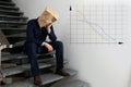 Man wearing paper bag with drawn sad face indoors and illustration of falling down chart. Economy recession concept Royalty Free Stock Photo