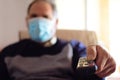 Man wearing protective mask during quarantine covid-19 using the remote control to change TV program. Isolation at home