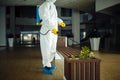 A man wearing protective suit is disinfecting a bench in an empty shopping mall with sanitizing spray. Cleaning up the public