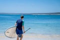 Man wearing rash guard with stand-up paddle board on a sandy beach near the ocean bay in Australia. SUP water sport activity Royalty Free Stock Photo