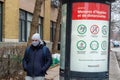 Man wearing a protective mask walking next to a sign showing Covid-19 safety guidelines