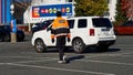 Man wearing a security guard jacket walkng amongst cars in a parking lot towards a grocery store Royalty Free Stock Photo