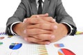 man wearing a suit sitting in a table full of charts with clasped hands