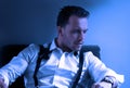 Man wearing tuxedo in hotel room, sitting in chair with loose tie