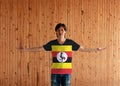 Man wearing Uganda flag color shirt and standing with arms wide open on the wooden wall background