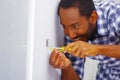 Man wearing white and blue shirt working on electrical wall socket wires using screwdriver, concentrated facial