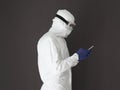 Man Wearing White Coverall Suit with Hood against Gray Wall Uses Cellphone.