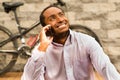 Man wearing white red business shirt sitting down, smiling and talking on mobile phone, bicycle standing behind leaning Royalty Free Stock Photo