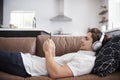 Man Wearing Wireless Headphones Lying On Sofa At Home Streaming From Mobile Phone Royalty Free Stock Photo
