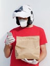 The man wears a kn95 mask and motorcycle helmet, holds paper bag